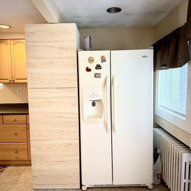 kitchen featuring white fridge with ice dispenser, radiator, and dark countertops