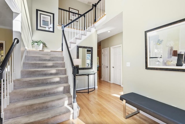 stairway with crown molding, a high ceiling, baseboards, and wood finished floors