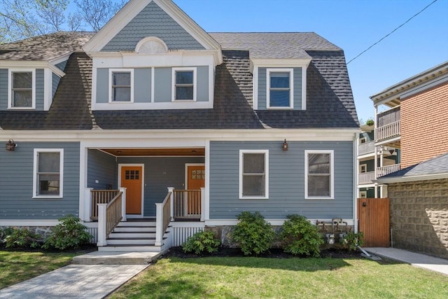 shingle-style home with a porch, fence, roof with shingles, and a front lawn