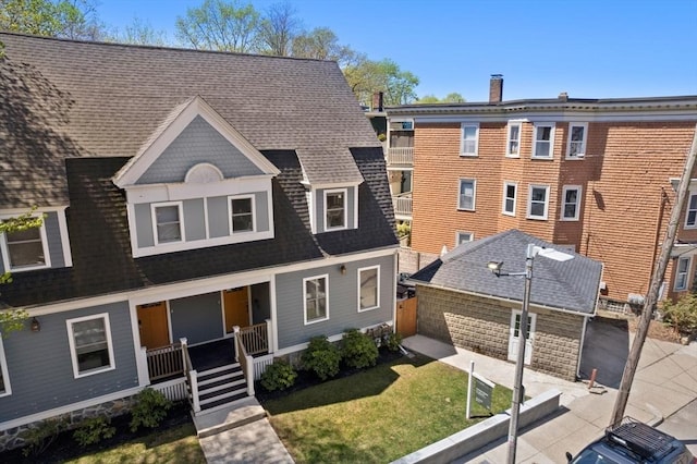 shingle-style home with roof with shingles, covered porch, and a front lawn