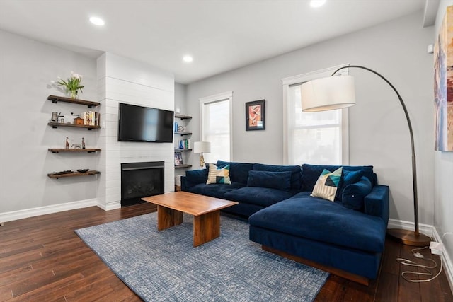 living area with baseboards, dark wood-style flooring, and a large fireplace