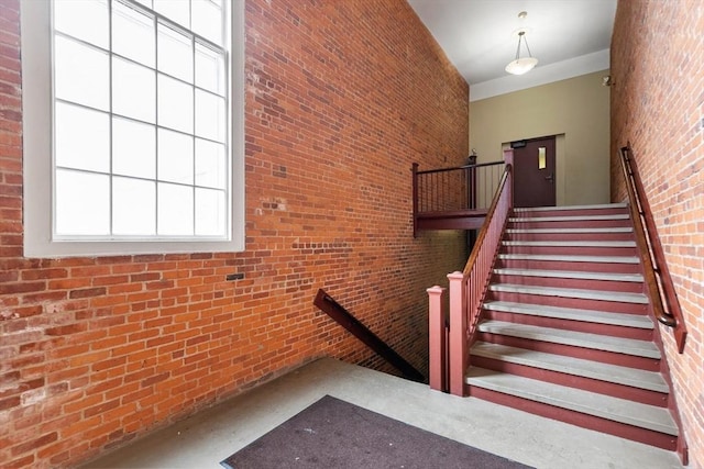 stairs featuring concrete floors, a high ceiling, and brick wall