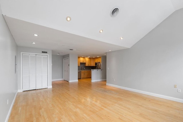 unfurnished living room featuring light wood-type flooring, vaulted ceiling, and sink