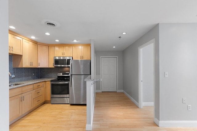 kitchen with stainless steel appliances, tasteful backsplash, light brown cabinetry, sink, and light stone counters