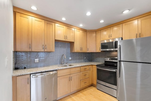 kitchen featuring stainless steel appliances, tasteful backsplash, light brown cabinetry, sink, and light hardwood / wood-style flooring