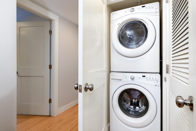 laundry room featuring stacked washing machine and dryer, light wood-style flooring, and baseboards