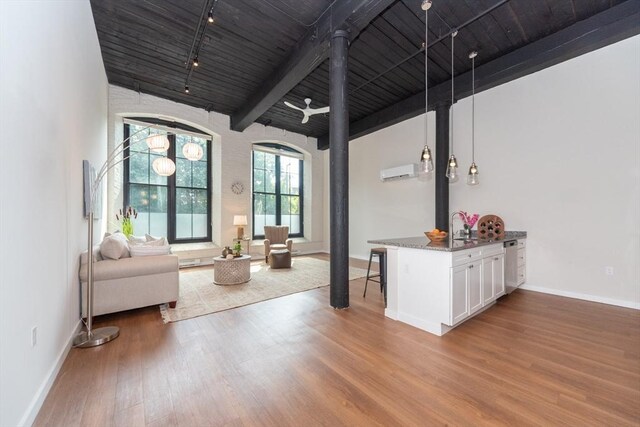 unfurnished living room with a wall unit AC, hardwood / wood-style floors, sink, beam ceiling, and a towering ceiling