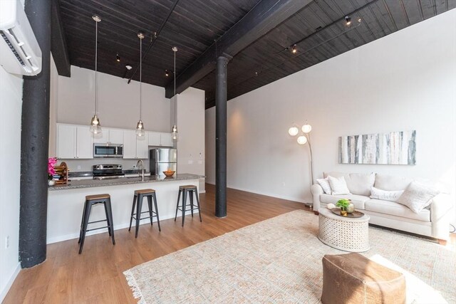 living room featuring a towering ceiling, a wall unit AC, light wood-type flooring, and sink