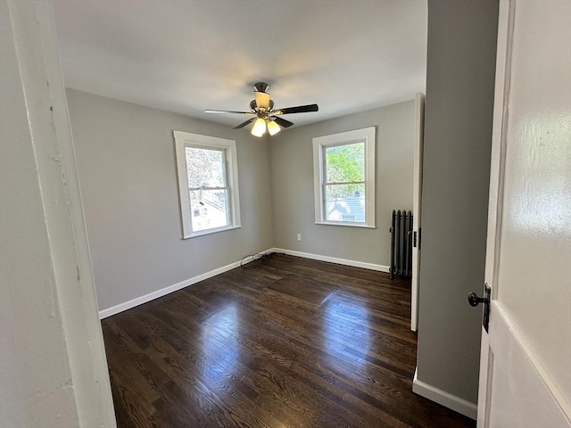 unfurnished room with a ceiling fan, baseboards, dark wood-style floors, and radiator heating unit