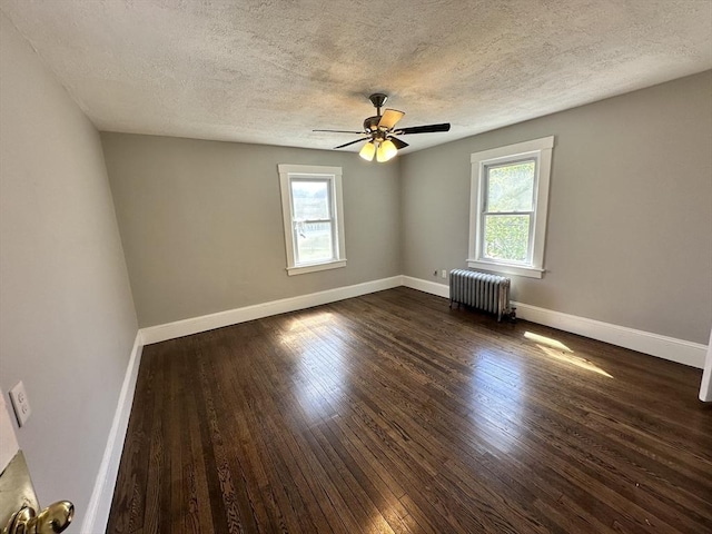 unfurnished room with plenty of natural light, a textured ceiling, dark wood finished floors, and radiator heating unit