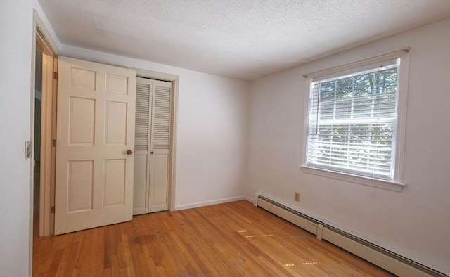 175 Knotty Pine Ln, Barnstable, MA 02632 - unfurnished bedroom with a baseboard heating unit, light wood-style flooring, a closet, and a textured ceiling
