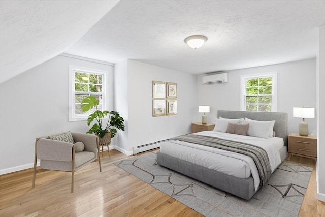 bedroom with a textured ceiling, lofted ceiling, a baseboard heating unit, light hardwood / wood-style flooring, and a wall mounted air conditioner