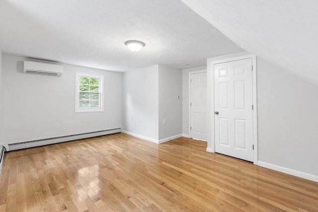 interior space with baseboard heating, light hardwood / wood-style floors, a wall mounted air conditioner, and lofted ceiling