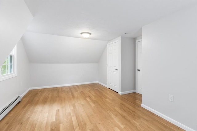 additional living space with a baseboard radiator, light wood-type flooring, and vaulted ceiling