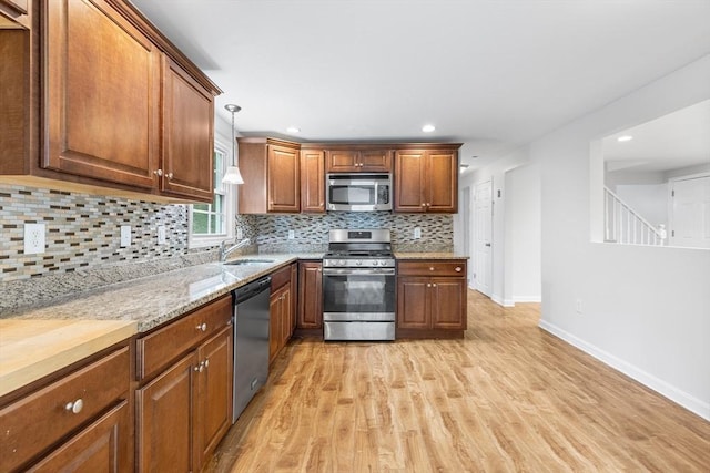 kitchen with decorative light fixtures, stainless steel appliances, sink, backsplash, and light wood-type flooring