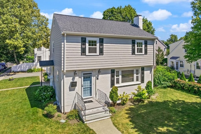 85 Loring Ave, Winchester, MA 01890 - view of front facade featuring a chimney, brick siding, a front yard, and roof with shingles