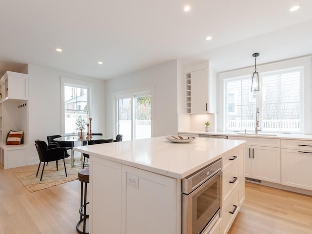 kitchen featuring white cabinetry, sink, decorative light fixtures, a kitchen island, and light wood-type flooring