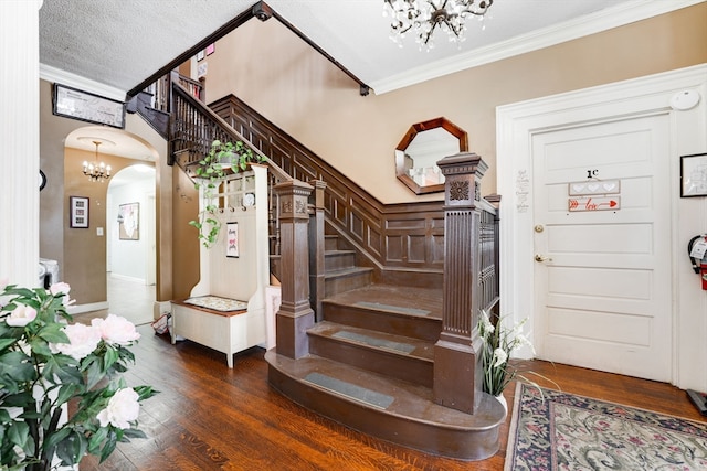 entrance foyer featuring a textured ceiling, dark hardwood / wood-style floors, ornamental molding, and a chandelier