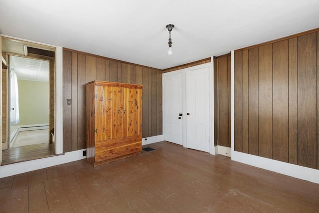 unfurnished bedroom with hardwood / wood-style flooring, wooden walls, multiple closets, and a baseboard radiator