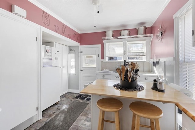 kitchen featuring crown molding, a breakfast bar area, light countertops, freestanding refrigerator, and white cabinets