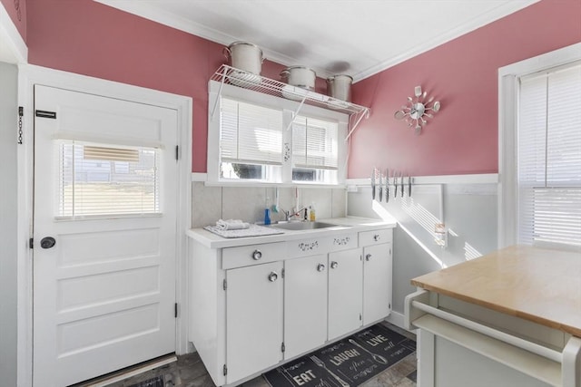 kitchen featuring wainscoting, white cabinets, light countertops, and a sink