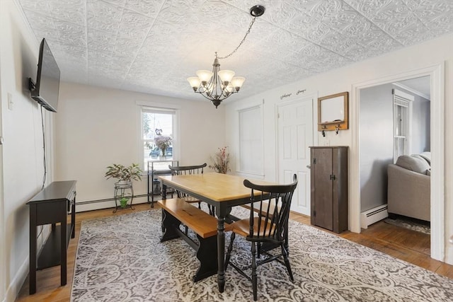 dining area featuring a notable chandelier, wood finished floors, an ornate ceiling, and a baseboard radiator