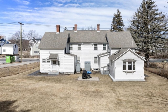 rear view of property featuring a lawn, entry steps, a shingled roof, and fence