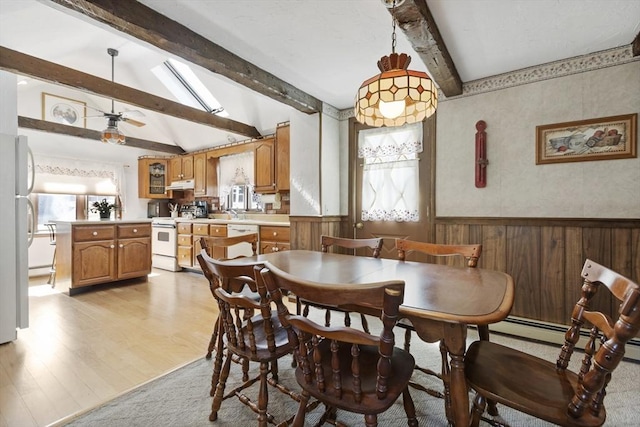 dining room featuring light wood finished floors, wooden walls, ceiling fan, lofted ceiling with skylight, and wainscoting