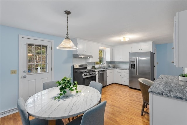 kitchen featuring white cabinets, appliances with stainless steel finishes, light wood-type flooring, sink, and decorative light fixtures