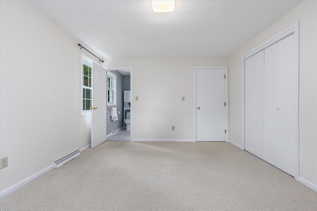 unfurnished bedroom featuring light carpet, ensuite bathroom, and a closet