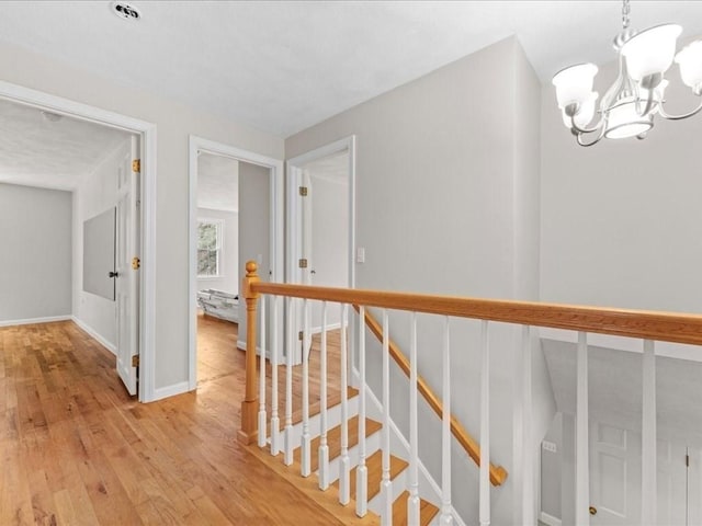 hall featuring a chandelier, baseboards, an upstairs landing, and light wood finished floors