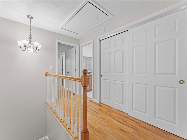 corridor with light wood finished floors, an inviting chandelier, attic access, an upstairs landing, and baseboards