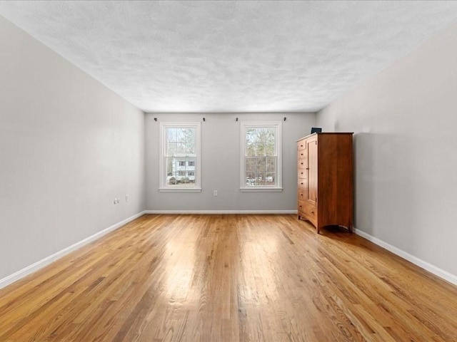 spare room featuring light wood-style flooring, baseboards, and a textured ceiling