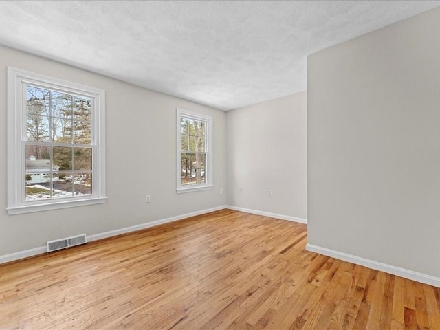 spare room featuring light wood-style floors, baseboards, visible vents, and a textured ceiling