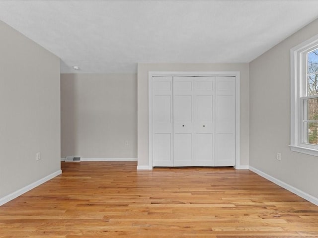 unfurnished bedroom featuring baseboards, a closet, visible vents, and light wood-style floors