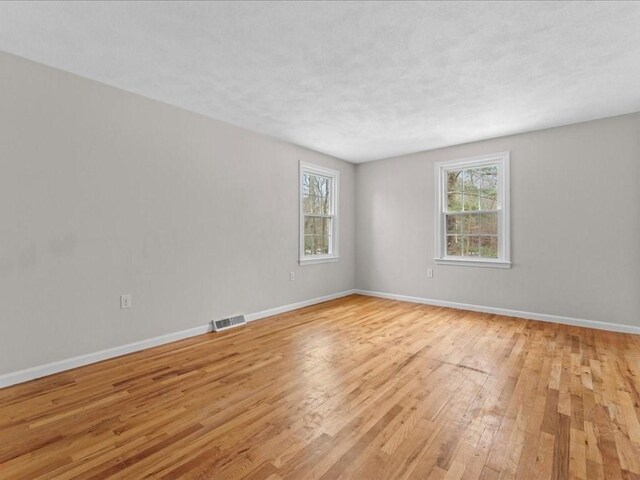 spare room with light wood-style floors, baseboards, visible vents, and a wealth of natural light