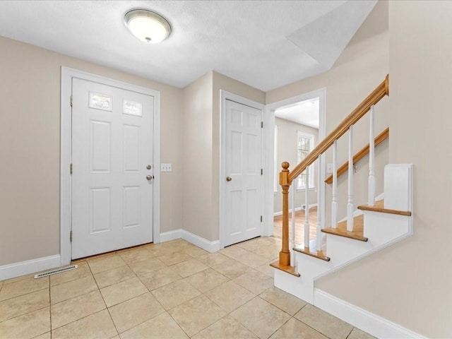 entryway with stairs, light tile patterned flooring, visible vents, and baseboards