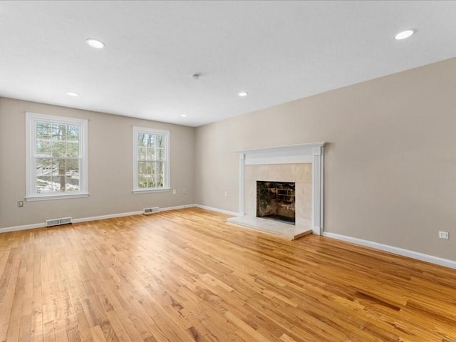 unfurnished living room featuring light wood-style floors, baseboards, visible vents, and a tile fireplace