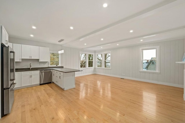 kitchen with hanging light fixtures, stainless steel appliances, beamed ceiling, kitchen peninsula, and white cabinets