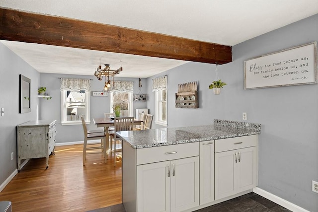 kitchen with light stone counters, beam ceiling, dark wood-type flooring, and white cabinets