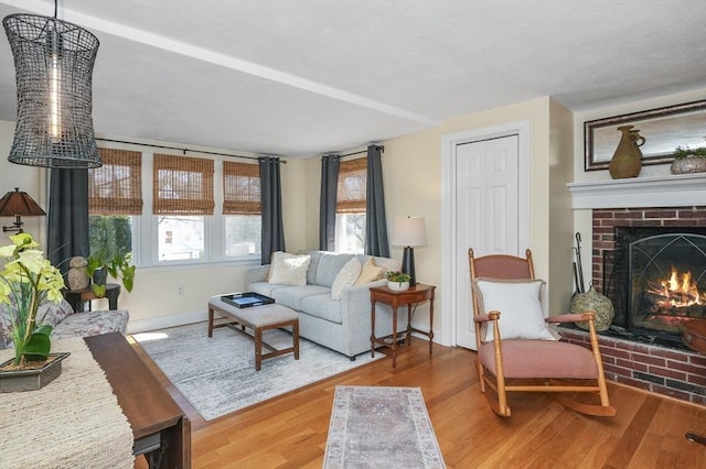 living room featuring baseboards, a brick fireplace, and wood finished floors