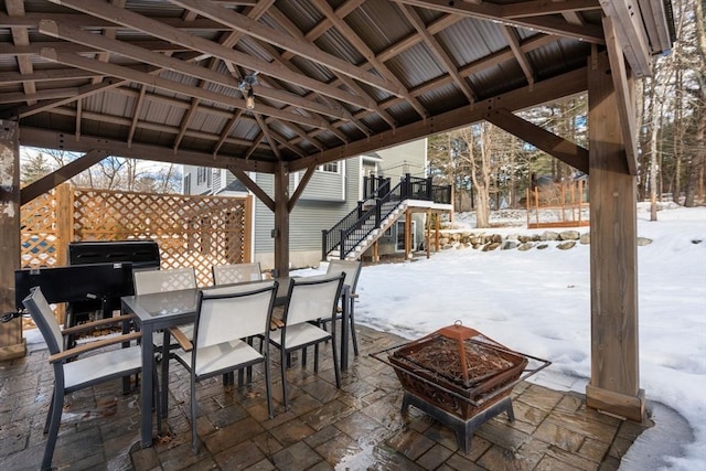 snow covered patio with an outdoor fire pit, stairs, outdoor dining area, and a gazebo