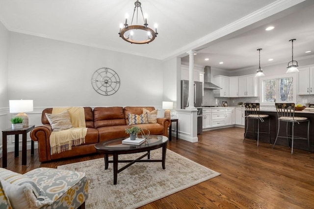 living area with dark wood finished floors, ornamental molding, ornate columns, a notable chandelier, and recessed lighting