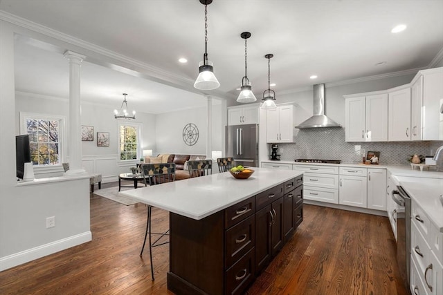 kitchen with wall chimney range hood, decorative columns, stainless steel appliances, and light countertops