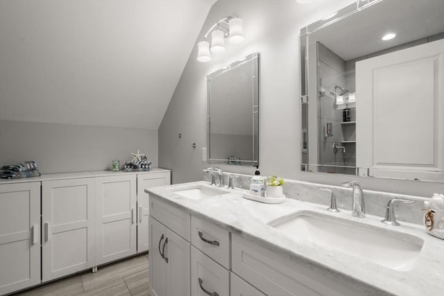 bathroom featuring lofted ceiling, double vanity, a sink, and walk in shower