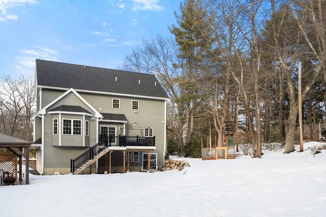 snow covered rear of property featuring a deck, a shingled roof, and stairway