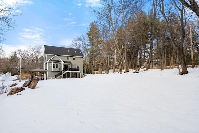 snow covered back of property with a wooden deck, a gazebo, and stairs