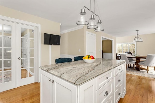 kitchen with white cabinetry, french doors, light wood-type flooring, light stone countertops, and pendant lighting