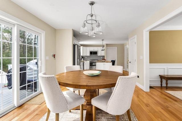 dining area with a chandelier, a decorative wall, a wainscoted wall, and light wood-style floors