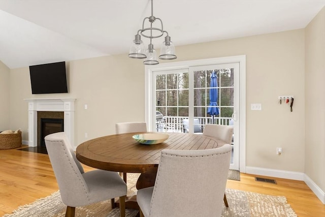 dining space with a fireplace, a notable chandelier, visible vents, light wood-style flooring, and baseboards